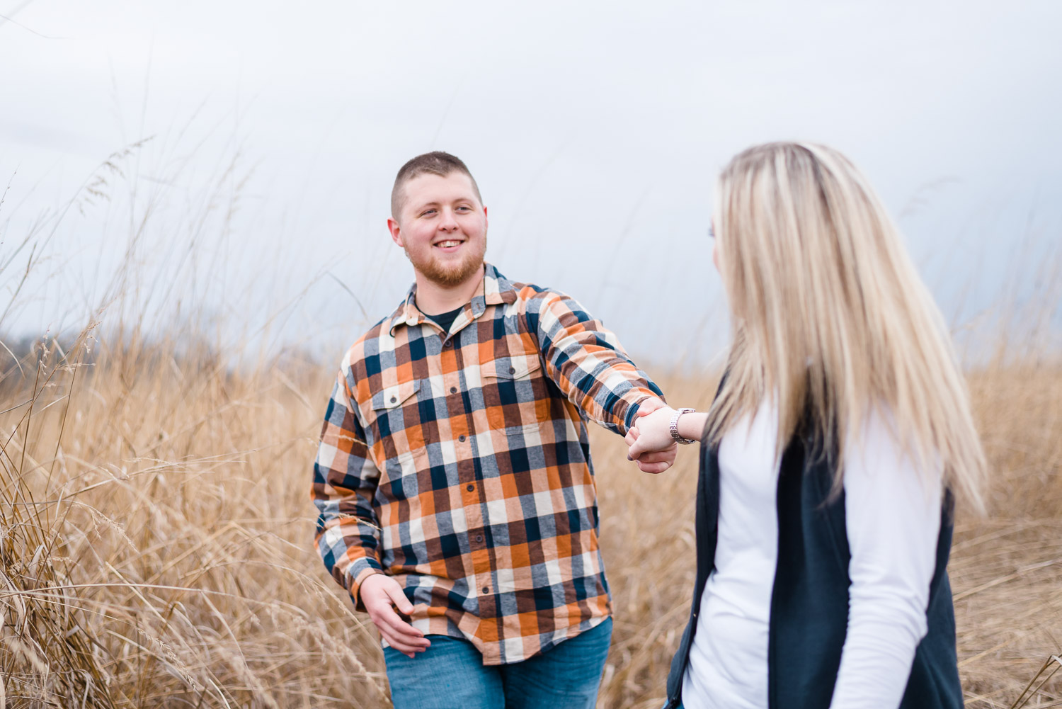 guy holding girl's hand in tall brown grass during engagement photo session