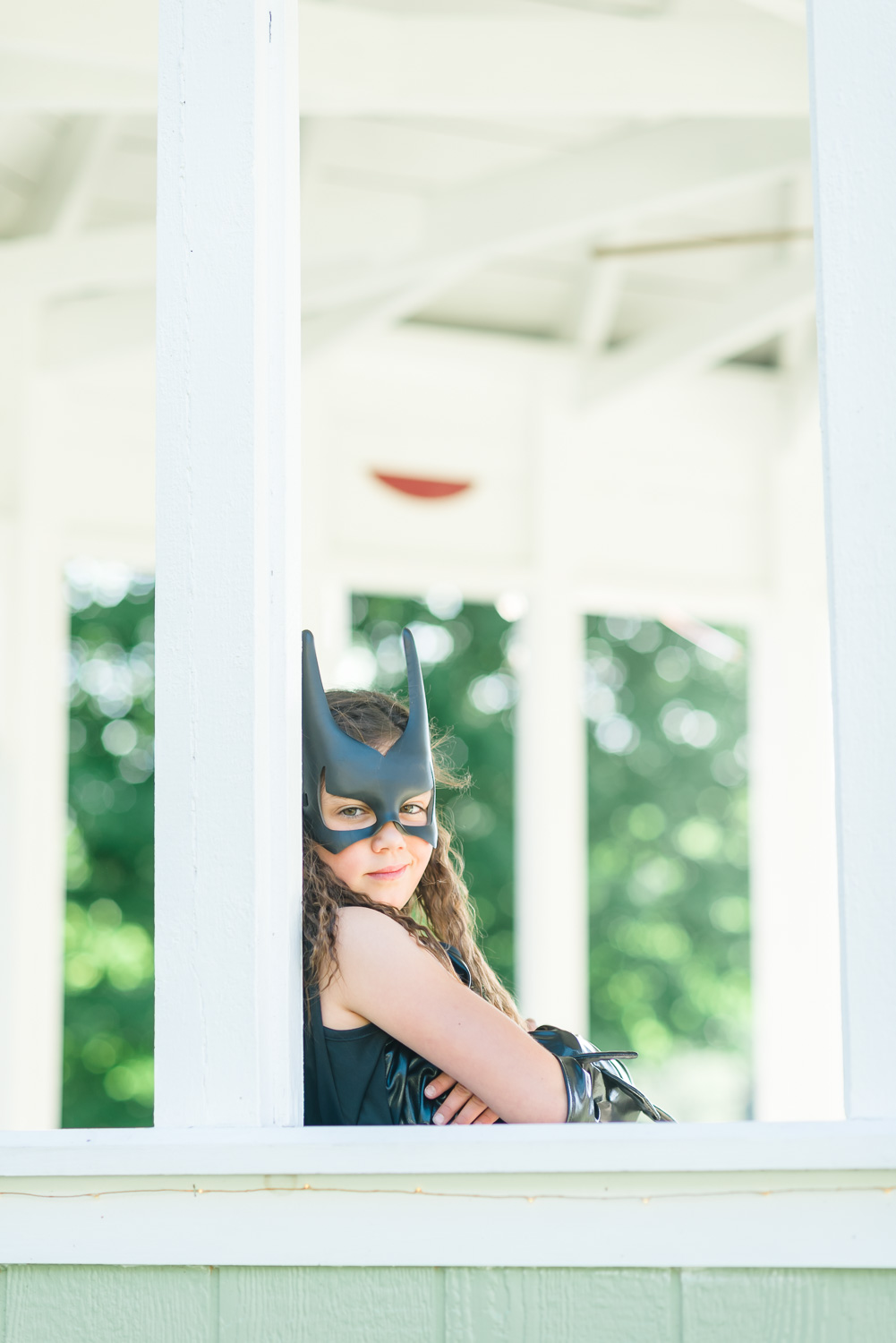 girl in batman costume and plastic batman mask sitting with arms crossed.