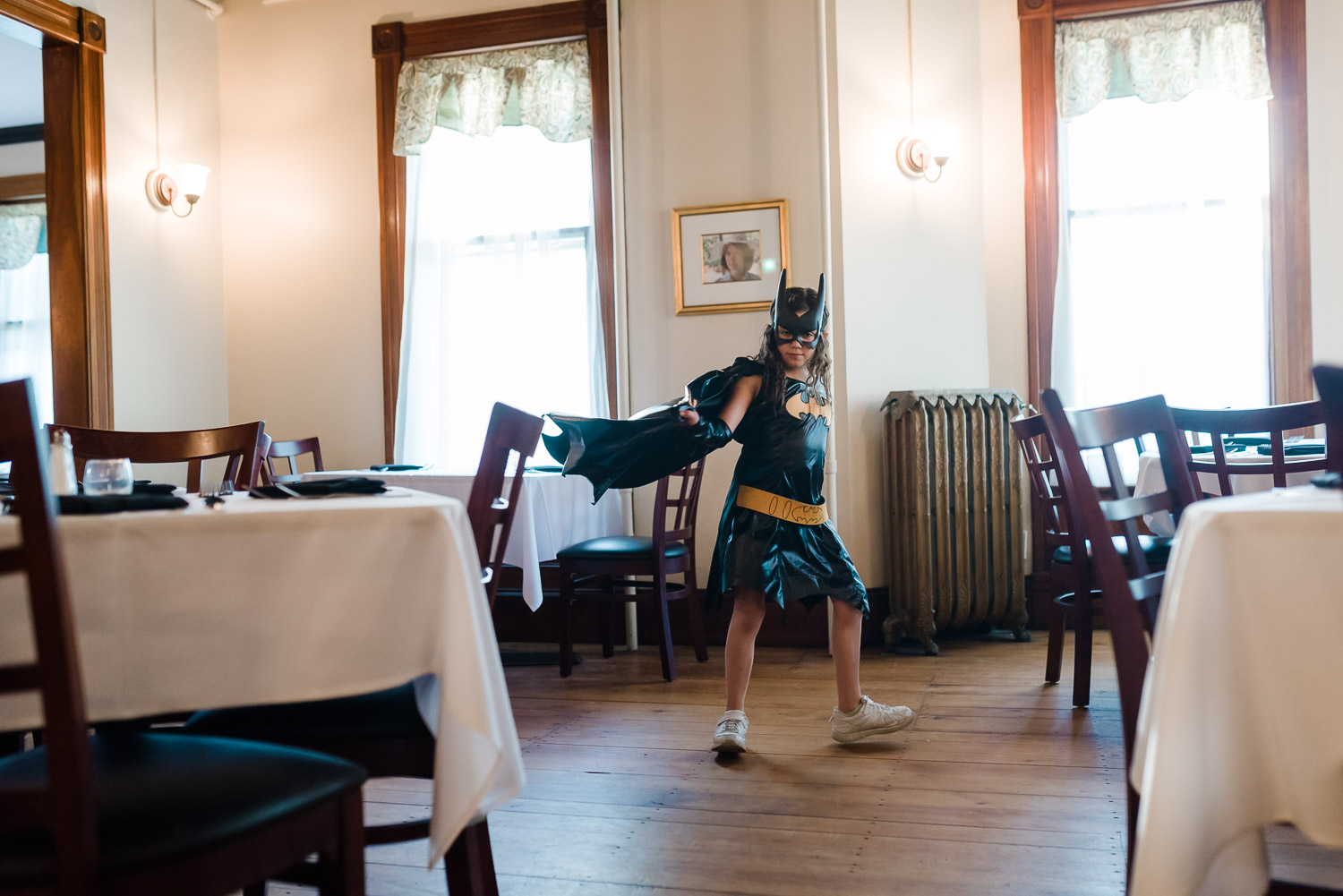 girl in batman costume walking with cape flying behind her in side of Tessie's Tavern