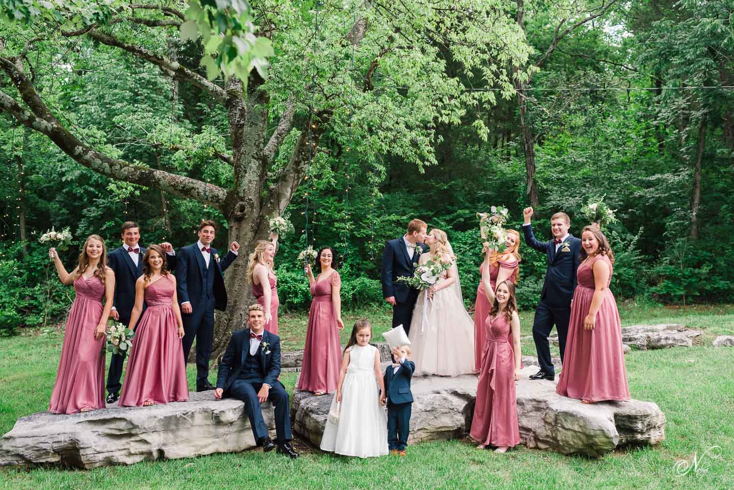 full wedding party standing outside on rocks with greenery in the background at the venue Chattanooga before the wedding ceremony.
