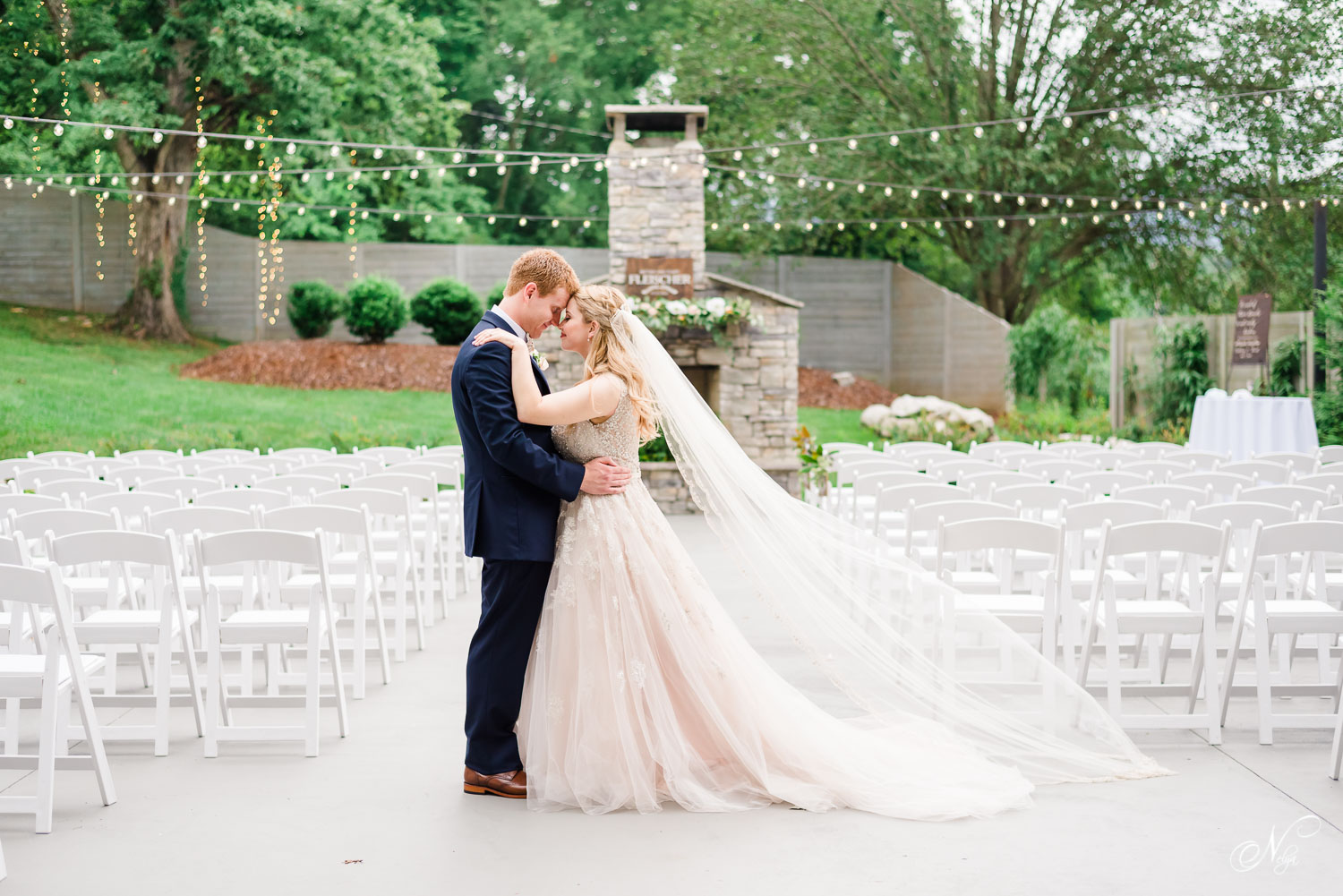 bride in stella York dress and cathedral length veil outside with groom in front of white chairs and an outdoor fireplace in Chattanooga TN