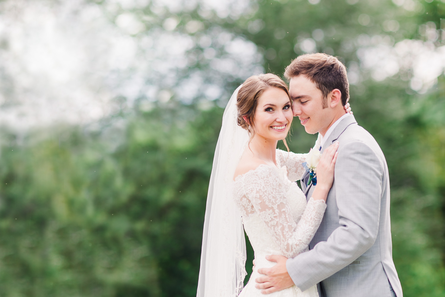 bride smiling at the camera in an off the shoulder lace sleeved Oleg Cassini wedding dress and groom in light gray suit just soaking up the moment with his new wife in Gatlinburg TN