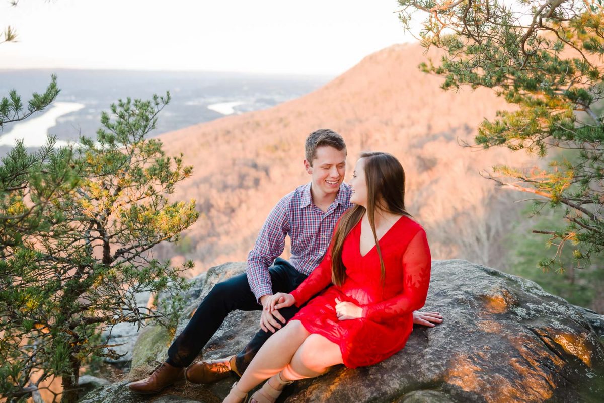 two people sitting on a rock between evergreen trees at sunset rock