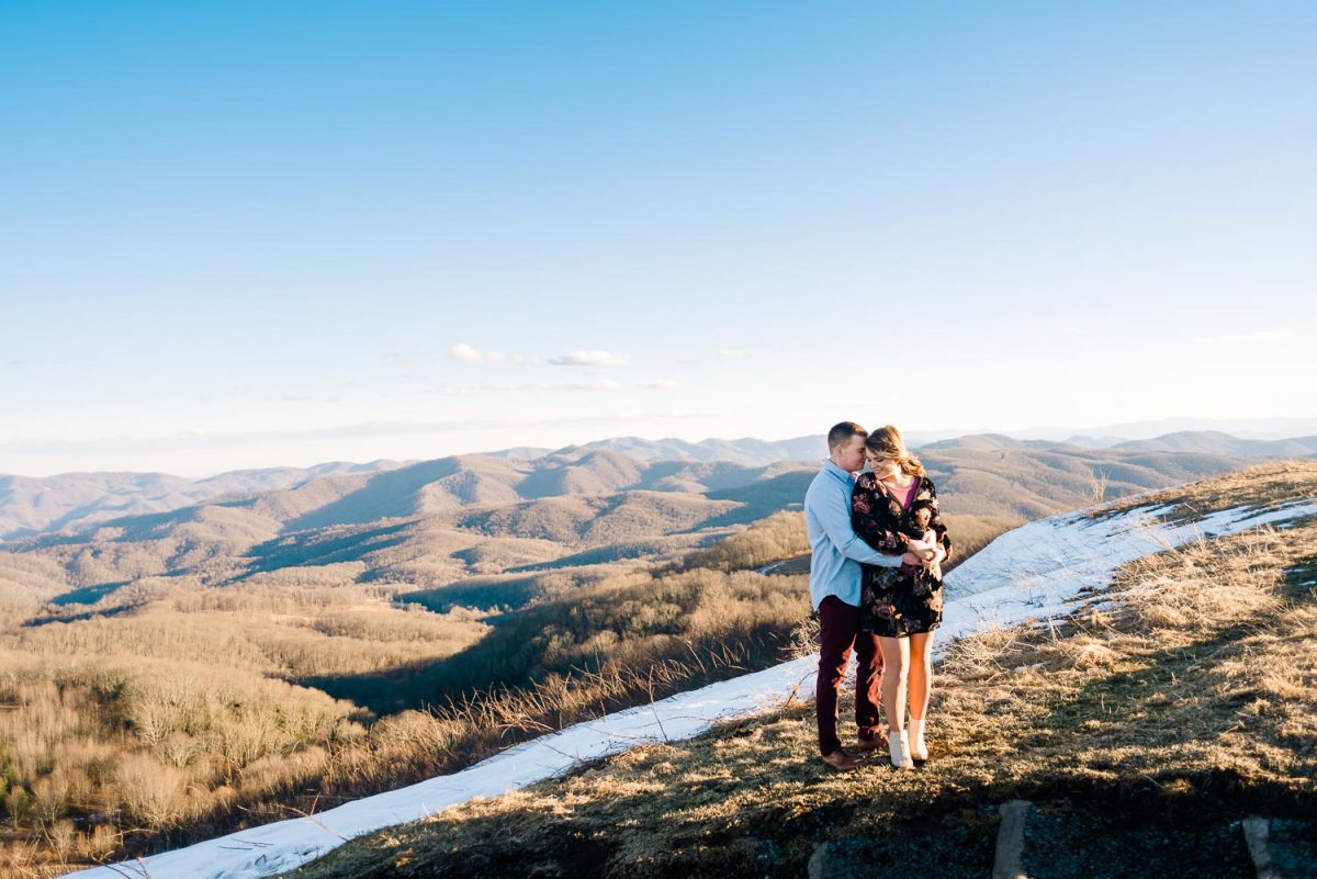 a couple on top of Max Patch wearing a short black floral dress and the guy wearing maroon pants and a blue button down