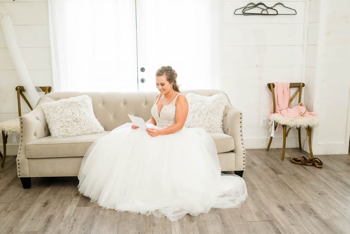 bride in white dress sitting on a couch reading a letter