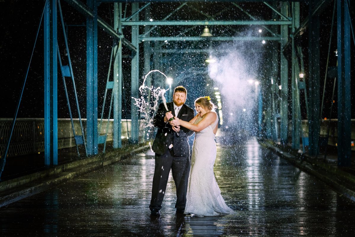 wedding couple popping champagne at night in the rain on the walnut street bridge in chattanooga
